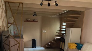 Een moderne woonkamer met een bank, twee ronde tafels, een houten bankje, een trap en een keukenhoek.