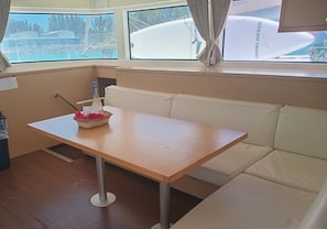 A cabin with a wooden table, a wicker basket with red flowers, a bottle, and a white cushioned bench.