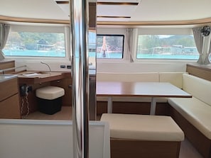 A boat interior with a dining area, a small kitchen, and a seating area with a view of the water. - Seychelles Sun-Soaked Sailing: A Pristine Beach Experience from Praslin (Baie Ste Anne)