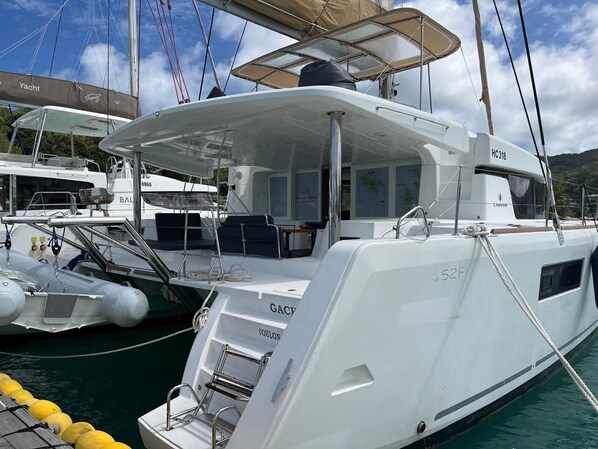 A white yacht docked at a marina with a covered deck area, a steering wheel, and a name 'GACY' on the side.
