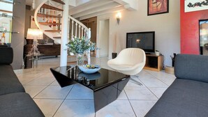 Un salon moderne avec une table basse noire, un fauteuil blanc, un téléviseur et un escalier.