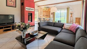 Un salon moderne doté d’un canapé d’angle, d’un téléviseur à écran plat, d’une cheminée et d’un coin repas agrémenté d’un lustre.