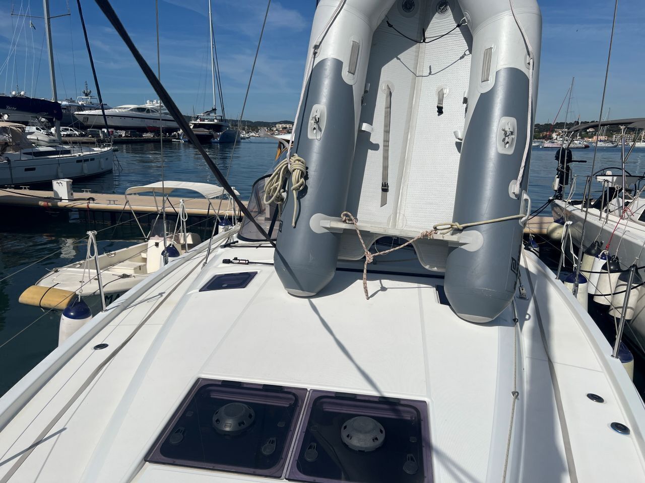 A sailboat docked at a marina with multiple boats, a white deck, and a lifebuoy.