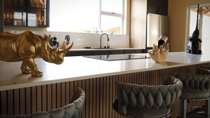 Cocina moderna con encimera blanca, un lavamanos y un ventanal. Hay dos sillas con diseño capitonado.