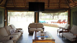 Una habitación con techo de paja, un sofá, una silla, una mesa de centro de madera y un televisor.