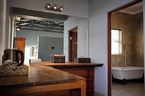 A bathroom with a bathtub, a shower, and a wooden vanity with a kettle and a suitcase.