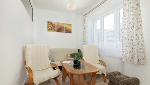 A room with a wooden coffee table, two armchairs, a small ottoman, and a window with floral curtains. - Cozy Apartment | Workspace (Kraków)