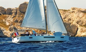 Un velero con varias velas, pasajeros y una costa rocosa al fondo.