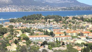 Eine Küstenstadt mit Gebäuden, einem Yachthafen und Bergen im Hintergrund.