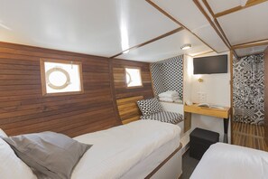 Une chambre de taille modeste, équipée de deux lits, d’un petit bureau, d’une télévision et d’un mur décoré d’un motif.
