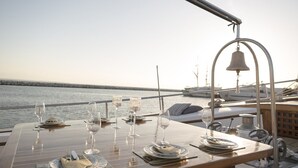 A table set for a meal with glasses and cutlery, a bell, and a view of the sea. - Sun-Kissed Sailing Adventure in Islas Sarónicas (Alimos)