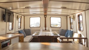 A dining area with a table set for four, two windows, and a central light fixture. - Sun-Kissed Sailing Adventure in Islas Sarónicas (Alimos)