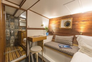 A compact room with a shower, a small desk, a bed with patterned bedding, and a potted plant. - Sun-Kissed Sailing Adventure in Islas Sarónicas (Alimos)