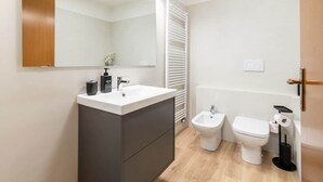 Un baño moderno con tocador, bidé, inodoro y espejo.
