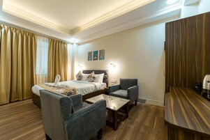 Habitación de hotel con una cama, dos sillones, una mesita pequeña, un escritorio de madera y una mesita de noche.