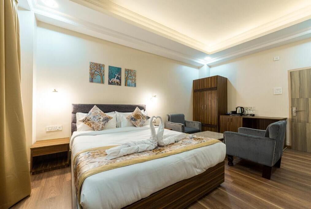 A hotel room with a large bed, a desk, a chair, and a wardrobe.