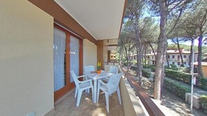 A balcony with a table and chairs, a potted plant, and a view of a residential area with trees and buildings. - Smart and Simple Flat (Lignano Sabbiadoro)