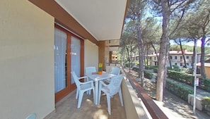 A balcony with a table and chairs, a potted plant, and a view of a residential area with trees and buildings. - Smart and Simple Flat (Lignano Sabbiadoro)