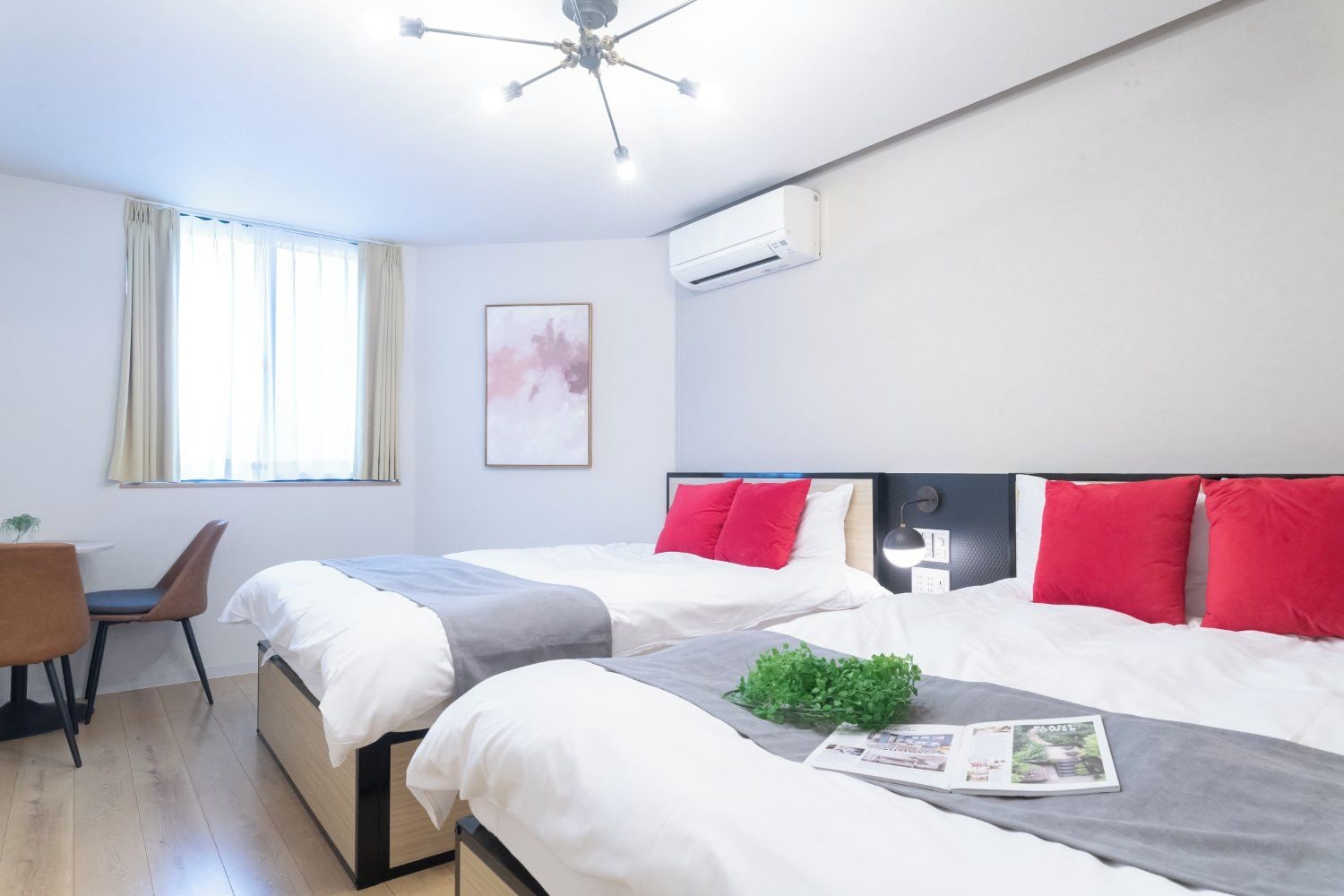 A hotel room with two beds, a desk, a chair, a ceiling fan, and an air conditioning unit.