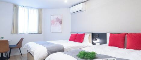 A hotel room with two beds, a desk, a chair, a ceiling fan, and an air conditioning unit.
