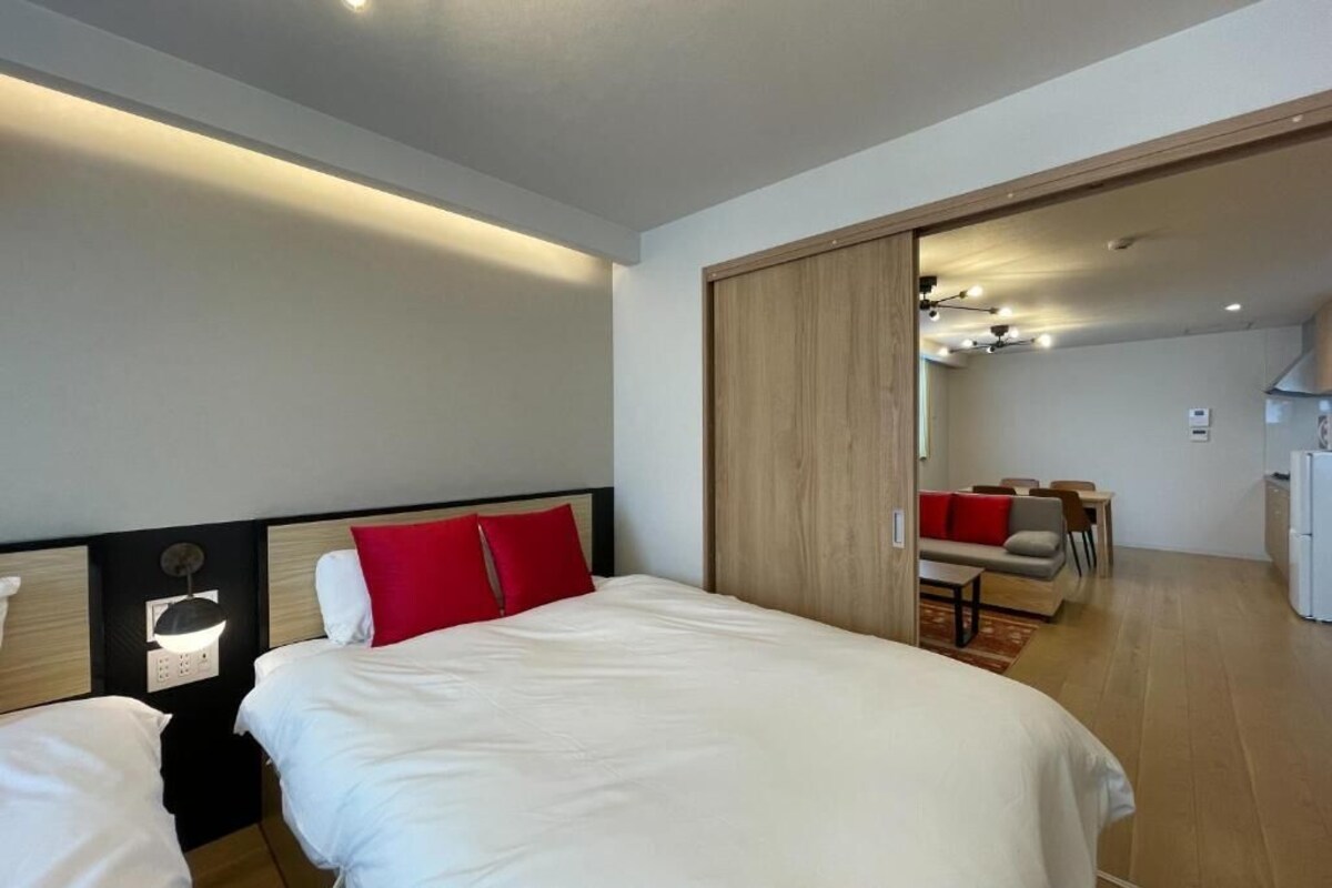 A hotel room with a bed, bedside table, and a view into the dining area.