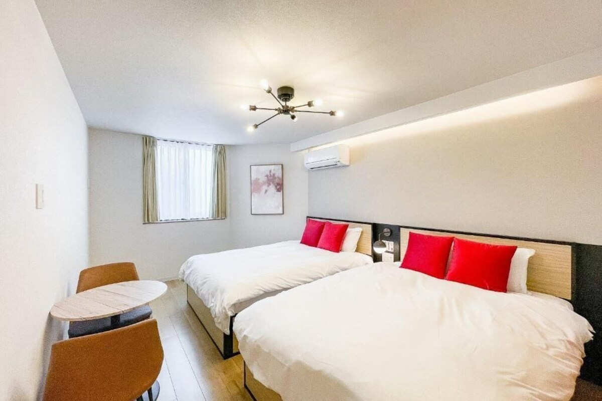A hotel room with two beds, a small table, and a ceiling light fixture.