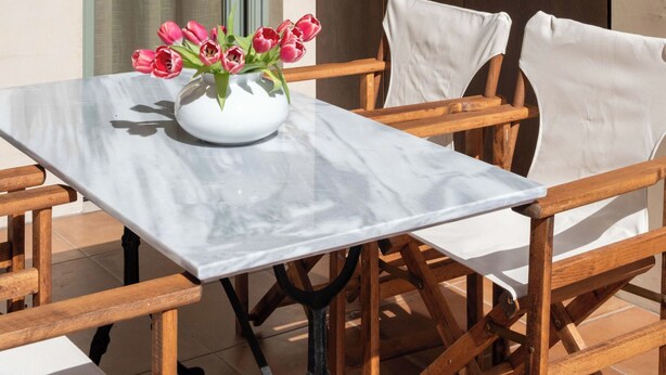 A table with a vase of flowers, wooden chairs, a window with curtains, and a wooden wall. - Ismini House (Chania)