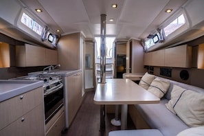 A compact kitchen with a stove, sink, and cabinets, a central dining table, and a sofa with cushions.