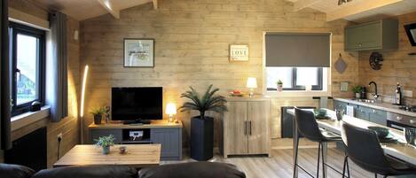 A modern living room with a TV, sofa, and dining area, connected to a kitchen with a bar stool.