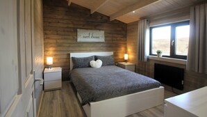 Un dormitorio con pared de madera, una cama con ropa de cama estampada, lámparas de noche, una ventana con cortinas y un letrero sobre la cama.