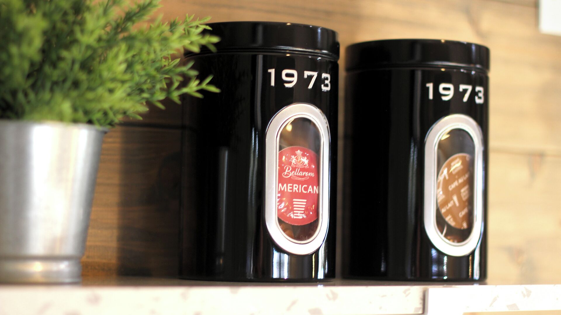 Two black containers with the year 1973 on them, placed on a shelf.