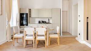 Cozinha moderna com armários brancos, mesa de jantar com quatro cadeiras e forno embutido.