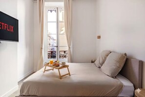 Ein Schlafzimmer mit einem Bett, einem Frühstücksbrett, einem Fernseher und einem Fenster mit Vorhängen.