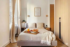 Ein ordentlich bezogenes Bett mit einem Frühstücksbrettchen, ein Nachttisch mit Lampe und ein an der Wand hängendes Kunstwerk.