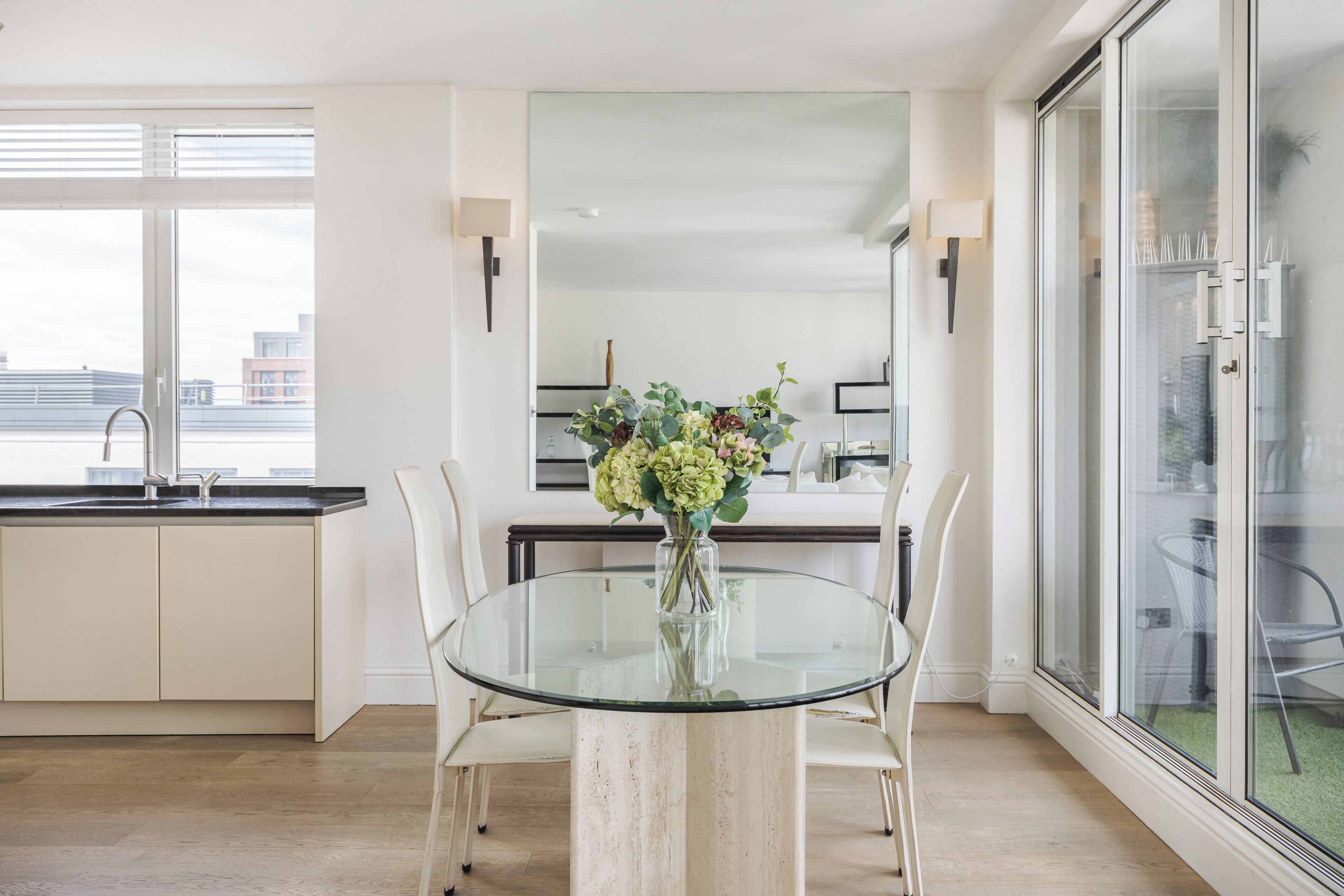A modern kitchen with a glass dining table, white cabinets, and a city view.