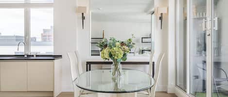 A modern kitchen with a glass dining table, white cabinets, and a city view.