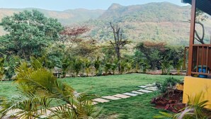 A well-maintained garden with a stone pathway, surrounded by lush greenery and a view of distant hills. - Mountain View Villa - Mulshi (Paud)