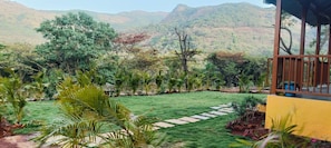 A well-maintained garden with a stone pathway, surrounded by lush greenery and a view of distant hills. - Mountain View Villa - Mulshi (Paud)