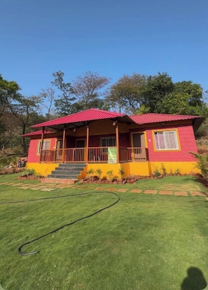 A two-story house with a red roof and yellow walls, surrounded by a well-maintained lawn and trees. - Mountain View Villa - Mulshi (Paud)