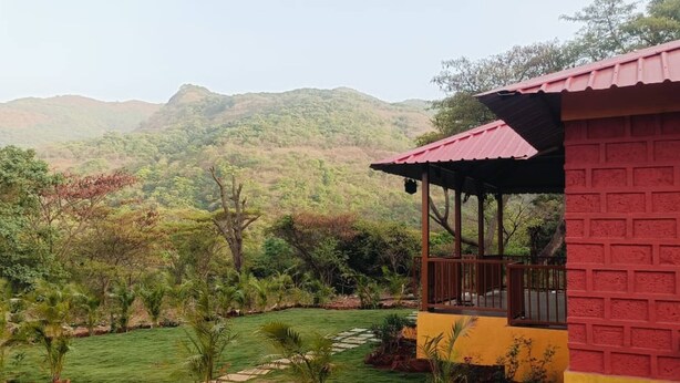 A building with a red brick exterior and a red roof, surrounded by lush greenery and hills in the background. - Mountain View Villa - Mulshi (Paud)
