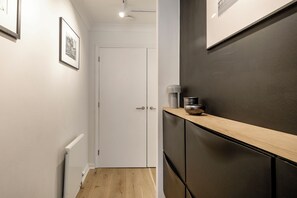 A narrow hallway with a white door, a radiator, and a shelf with a kettle. - Modern by the Market, by Veeve (London)