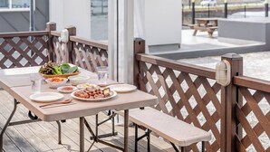 Een tafel gedekt met eten en drinken, een houten bank en een houten spijlenhek.