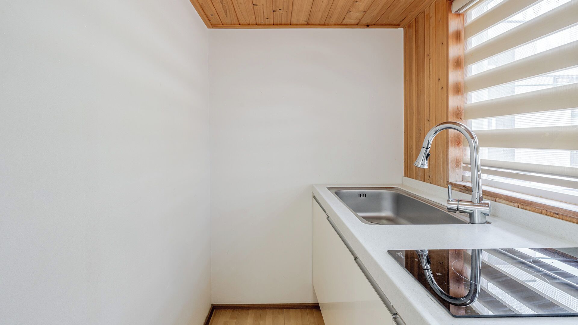 Cocina con un lavamanos de acero inoxidable, techo de madera y una ventana con persianas.