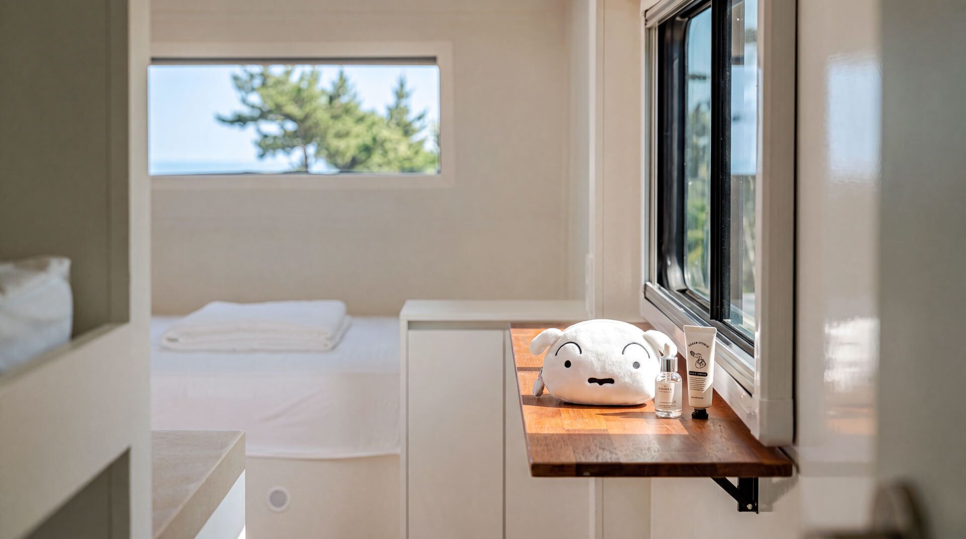A bedroom with a bed, a window, a bedside table with toiletries, and a view of trees outside.