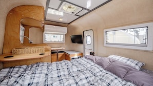 Een compact camperinterieur met een bed, een klein bureau, een spiegel en een televisie.