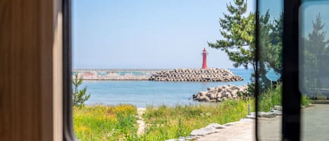 A view of a lighthouse and breakwater from a window, with a clear sky and calm sea.
