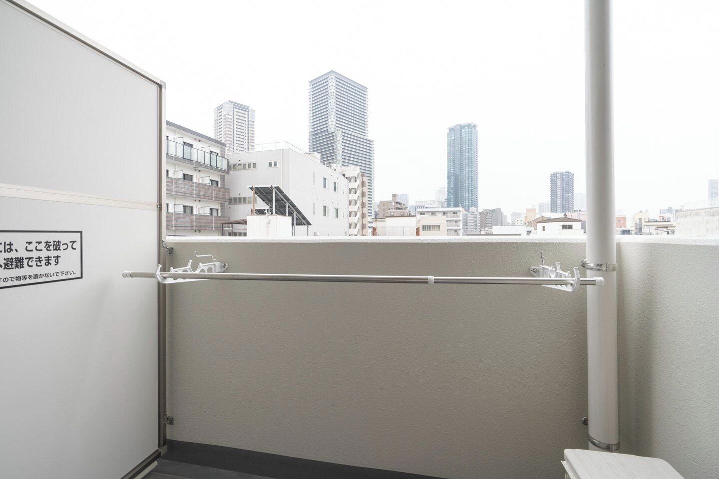 A balcony with a metal railing, a view of city buildings, and a sign with Japanese text.