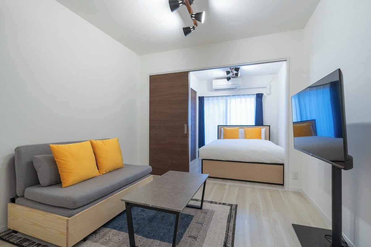 A modern hotel room with a sofa, a bed, a TV, and a ceiling fan.