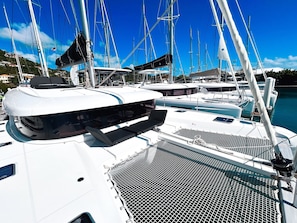 A marina with multiple sailboats docked, featuring a white deck with a netted area and a cabin structure.