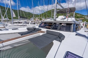 Ein Yachthafen mit mehreren Segelbooten, einem überdachten Deck mit Sitzgelegenheiten und einer bergigen Kulisse.